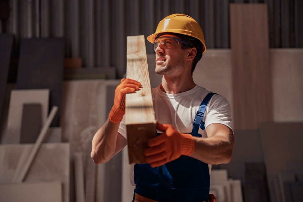 Handsome man carrying timber wood plank at construction site